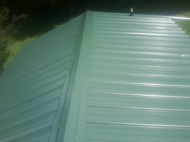 New green metal panels meeting at the ridge of a roof — Flat Roof Repair work by our crew in Ruffin