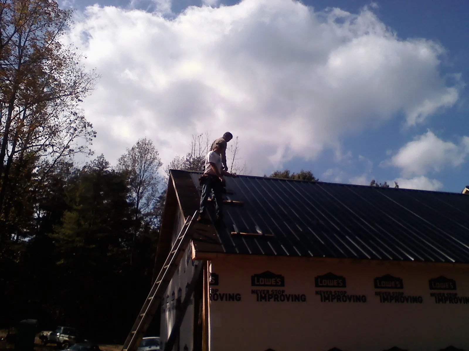 Roofer fastening dark metal panels high against a cloudy sky, from a Roof Inspection job in Ruffin