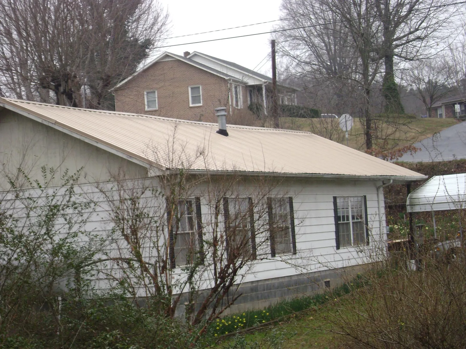 Tan metal roof on a white sided house set into a hillside — Commercial Roofing by Roofing Brothers in Ruffin