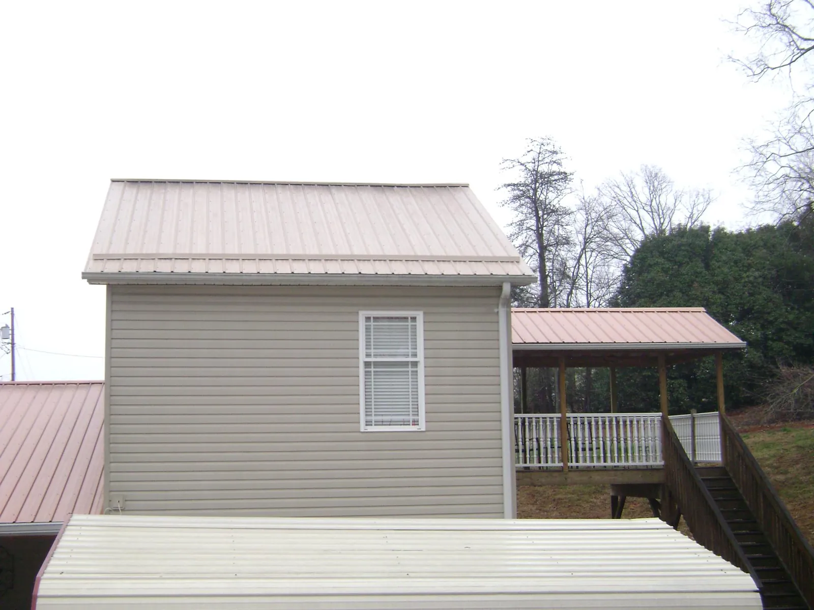 Tan metal roofs on a two story addition and attached porch, from a Roof Replacement job in Ruffin